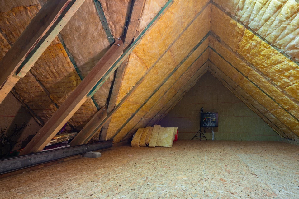 Ouvrier en combinaison bleue installant de l'isolant thermique jaune dans les combles d'une habitation