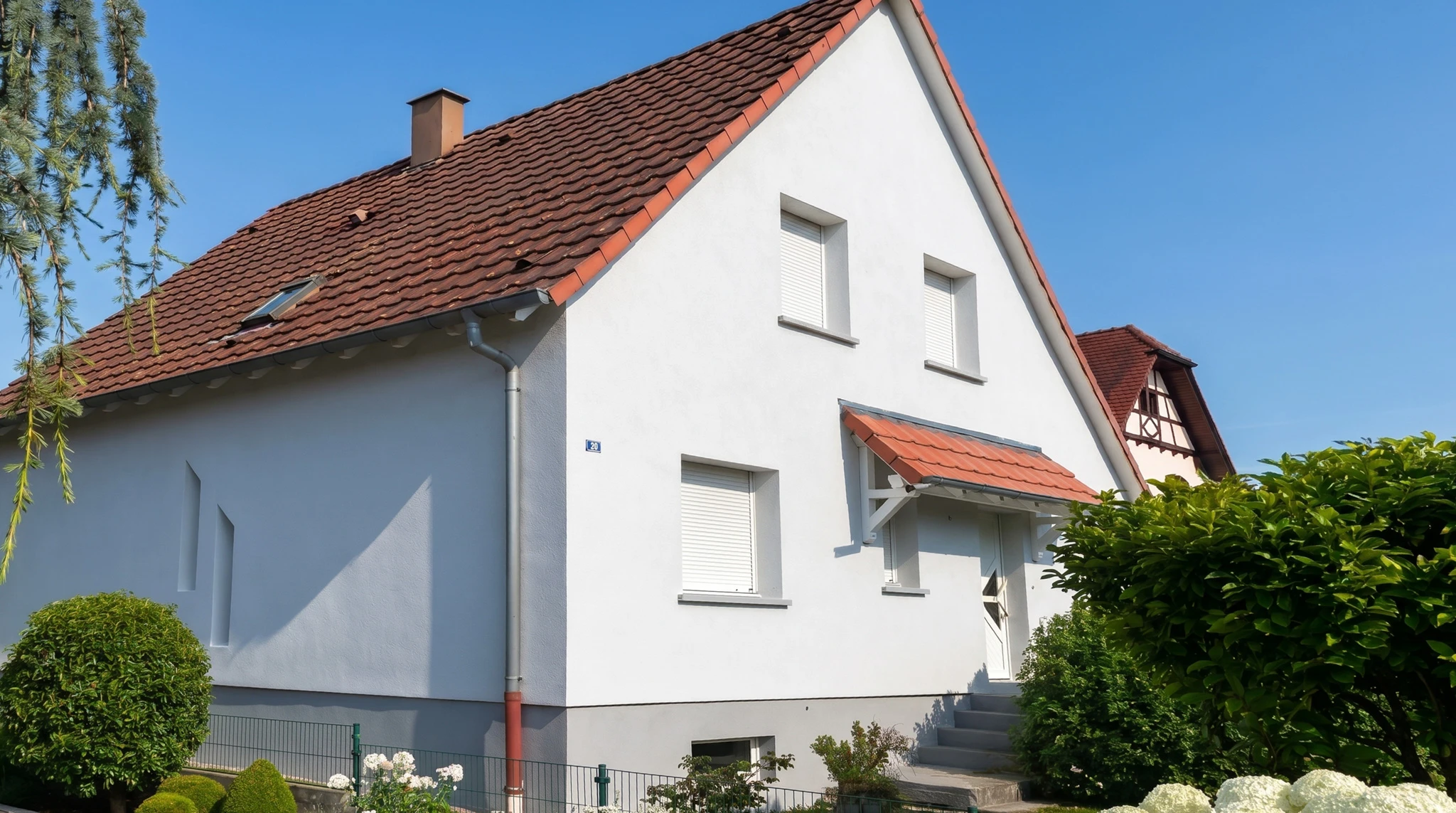 Extérieur d'une habitation, personne appliquant un revêtement mural texturé beige sur façade à l'aide d'un rouleau de peinture à manche télescopique