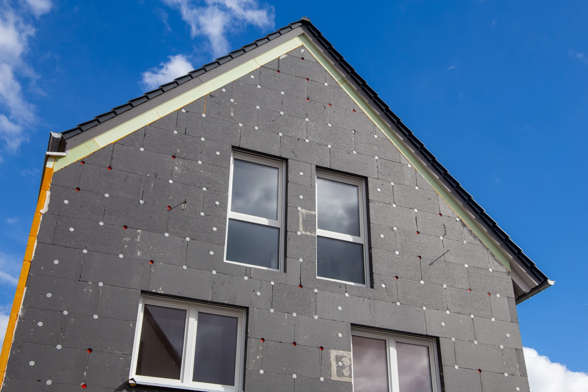 Façade extérieure d'habitation avec mur crépi beige, fenêtre à quatre carreaux avec encadrement blanc et appui de fenêtre en saillie