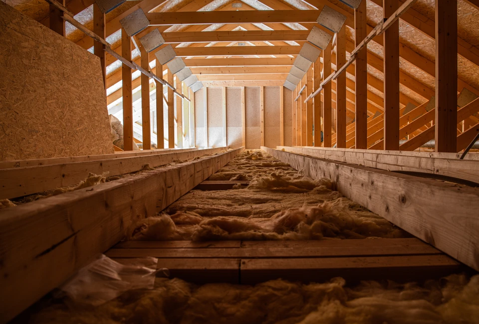 Ouvrier en combinaison bleue installant de l'isolant thermique jaune dans les combles d'une habitation