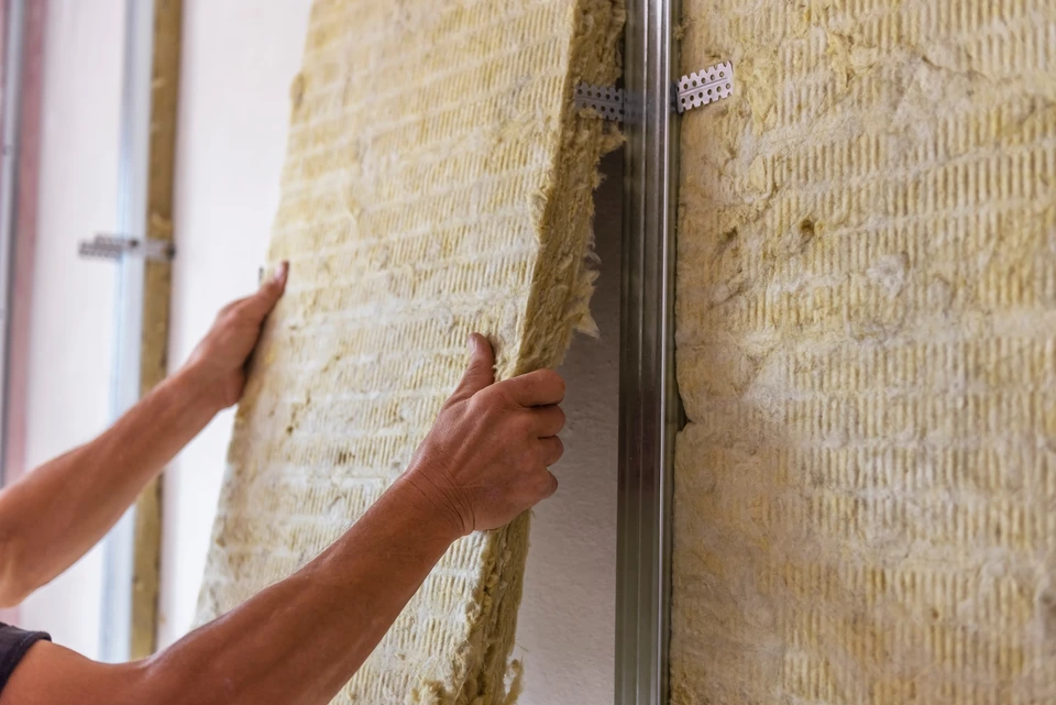 Ouvrier en combinaison blanche et masque respiratoire installant des panneaux d'isolation thermique dans les combles d'une habitation