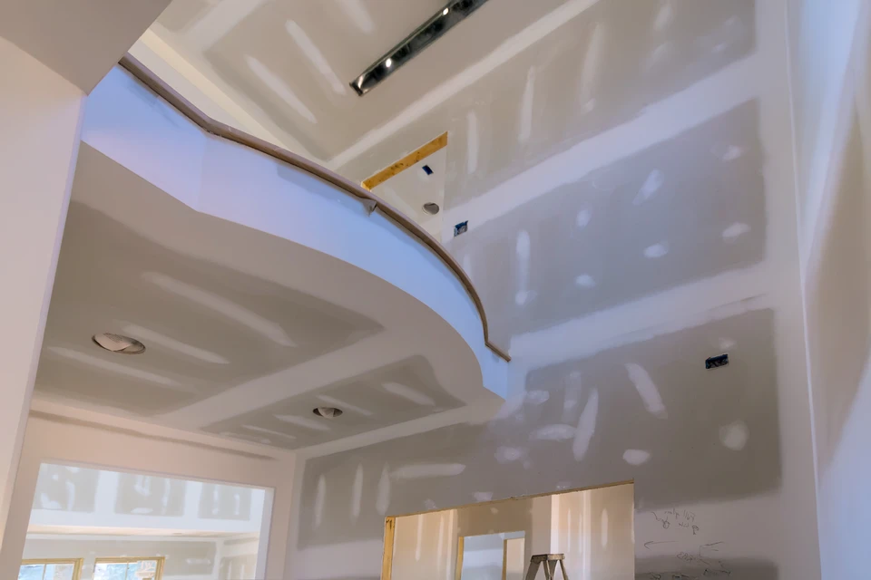 Un ouvrier en vêtements blancs applique de l'enduit sur un mur intérieur à l'aide d'une taloche métallique